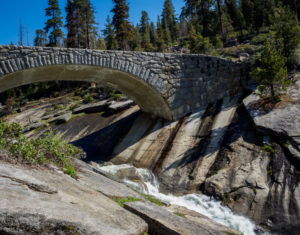 Image of water coursing over a large granite outcrop under a bridge