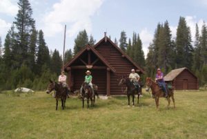 An image of four people on horseback in front of the Hockett Meadows Ranger Station
