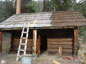 Image of cabin with a hand-made wooden ladder in front and partially-restored roof shingles